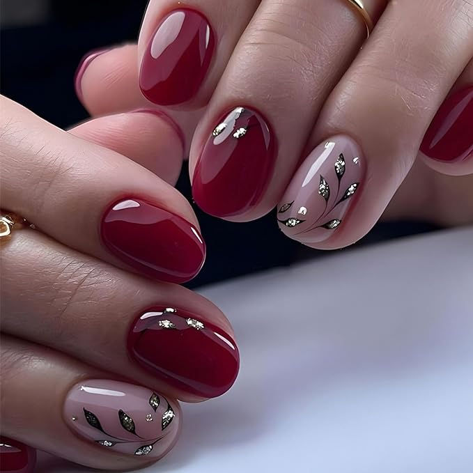 Elegant Chic Nail Design with Deep Red Polish, Beige Accents, and Metallic Leaf Motifs.