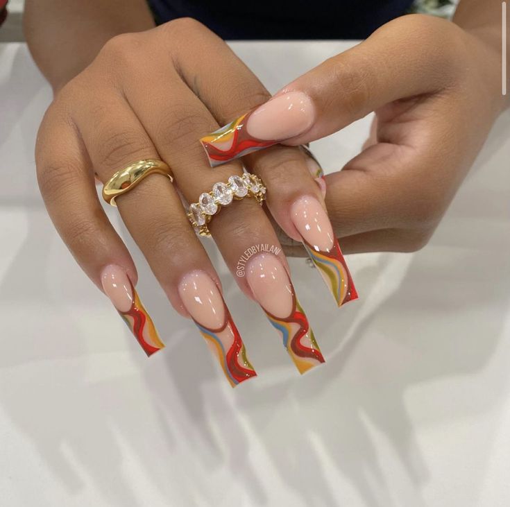 Chic Vibrant Acrylic Nail Design with Glossy Nude Base and Bold Swirling Tips, Accessorized by Elegant Gold and Diamond Rings.