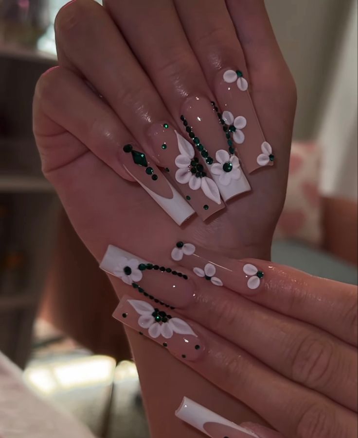 Elegant Floral Nail Design with Intricate White Flowers and Green Gemstones.