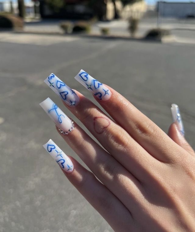 Trendy Long White Square Nail Design with Intricate Blue and Red Artwork and Decorative Embellishments.