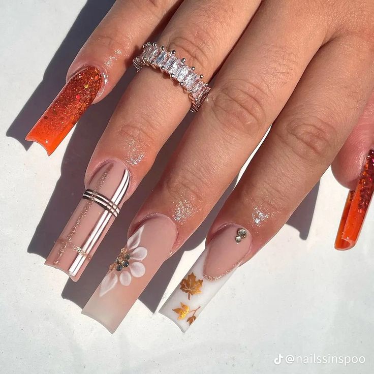 Vibrant and Elegant Fall Nail Design with Glittery Orange Tips and Floral Motifs.