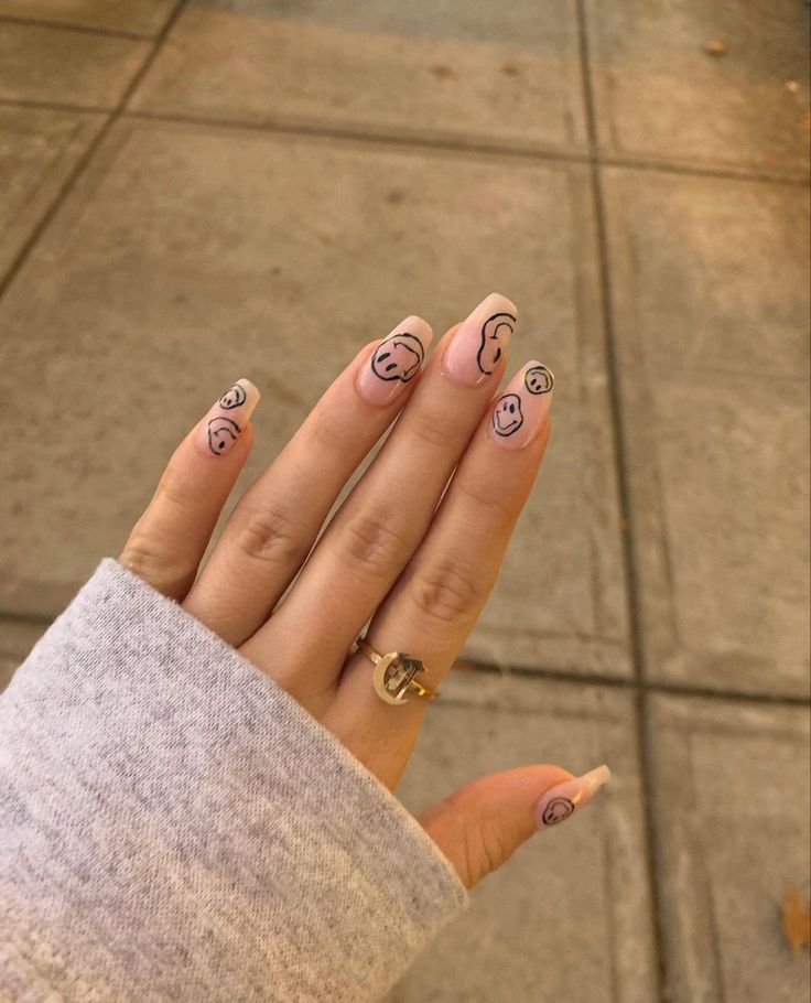 Playful Nail Design: Neutral Base with Hand-Drawn Smiley Faces and Wavy Lines in Soft Pink and Black.