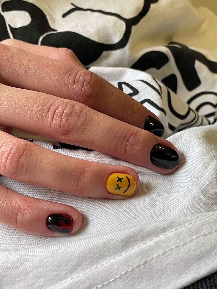 Bold and Playful Nail Design: Edgy Black and Red with Cheerful Yellow Smiley Accent.