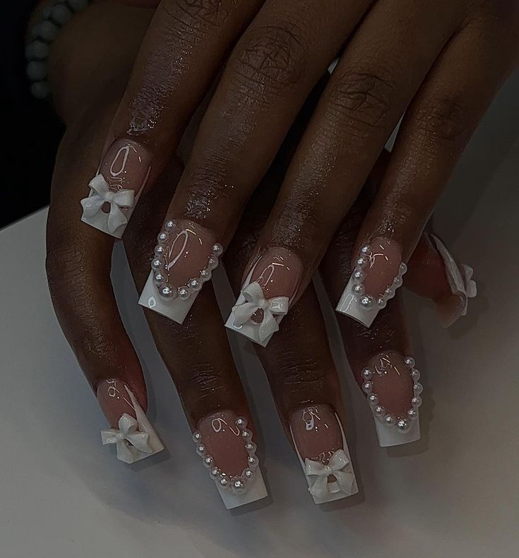 Sophisticated Nail Design with Glossy Nude and White Tips, Adorned with Bows and Pearls.