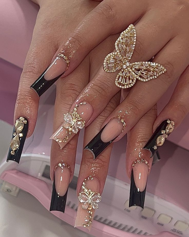 Luxurious Black and Nude Stiletto Nail Design with Sparkling Gems and Floral Accents.