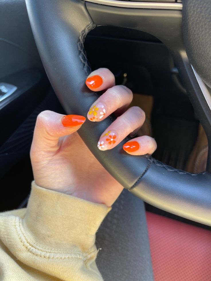 Cheerful Vibrant Orange Nails with Delicate Floral Designs for a Playful Look.