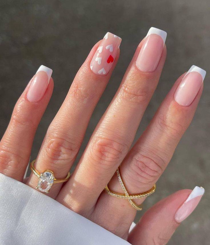 Romantic French Tip Manicure with Heart Accents and Dainty Gold Rings.