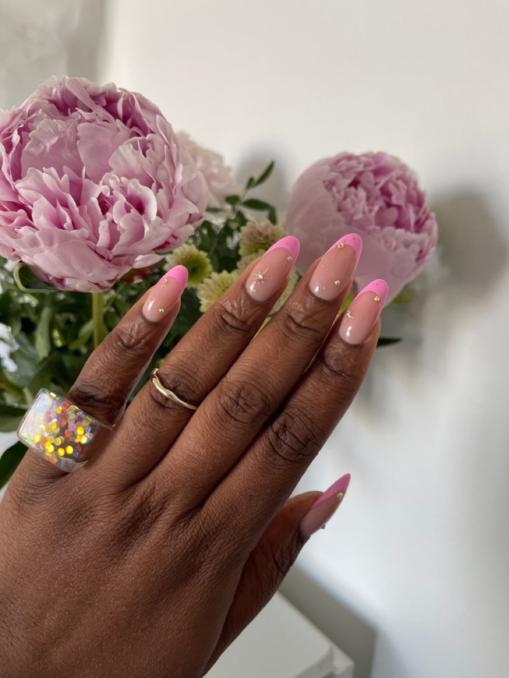 Playful Nail Design: Soft Nude Base with Bright Pink Tips and Glamorous Sparkling Embellishments Framed by Lush Peonies.