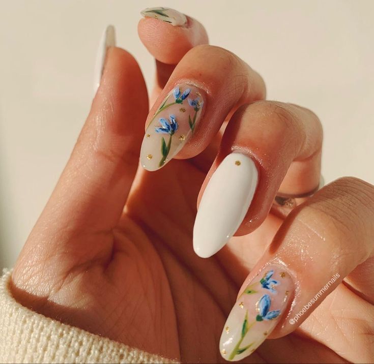 Elegant Floral Nail Design with Blue Flowers, White Accents, and Gold Dots on a Nude Background.