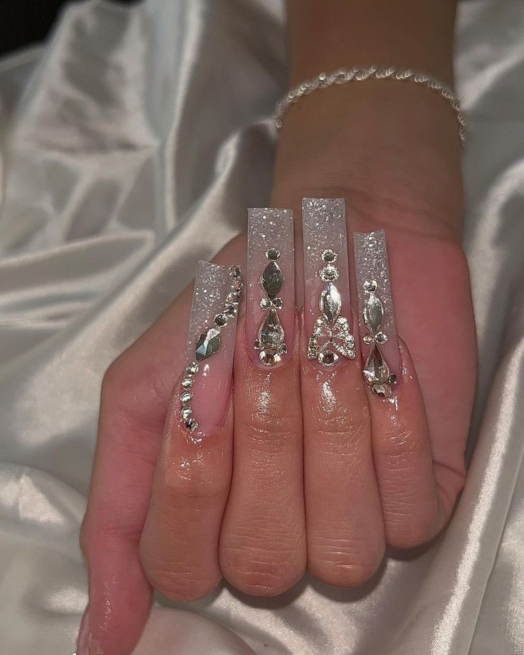 Elegant Glittering Nail Design with Elongated Clear Nails and Silver Embellishments.