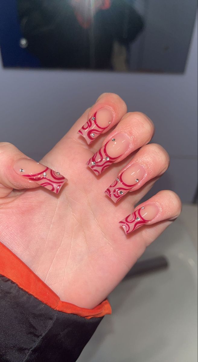 Vibrant Red Swirl Nail Design on Nude Base with Rhinestones for a Bold, Elegant Statement.