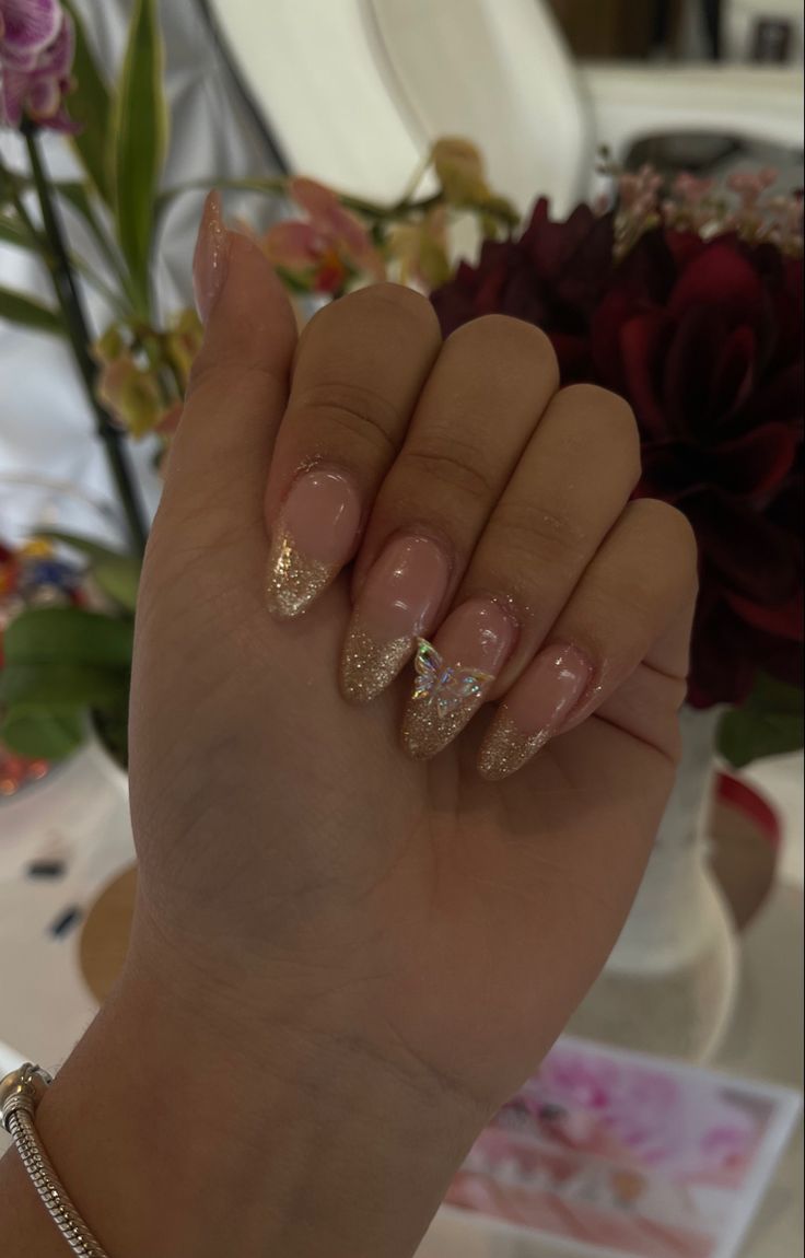 Chic Elegant Nail Design: Nude Base with Shimmering Gold Tips and Butterfly Embellishment.