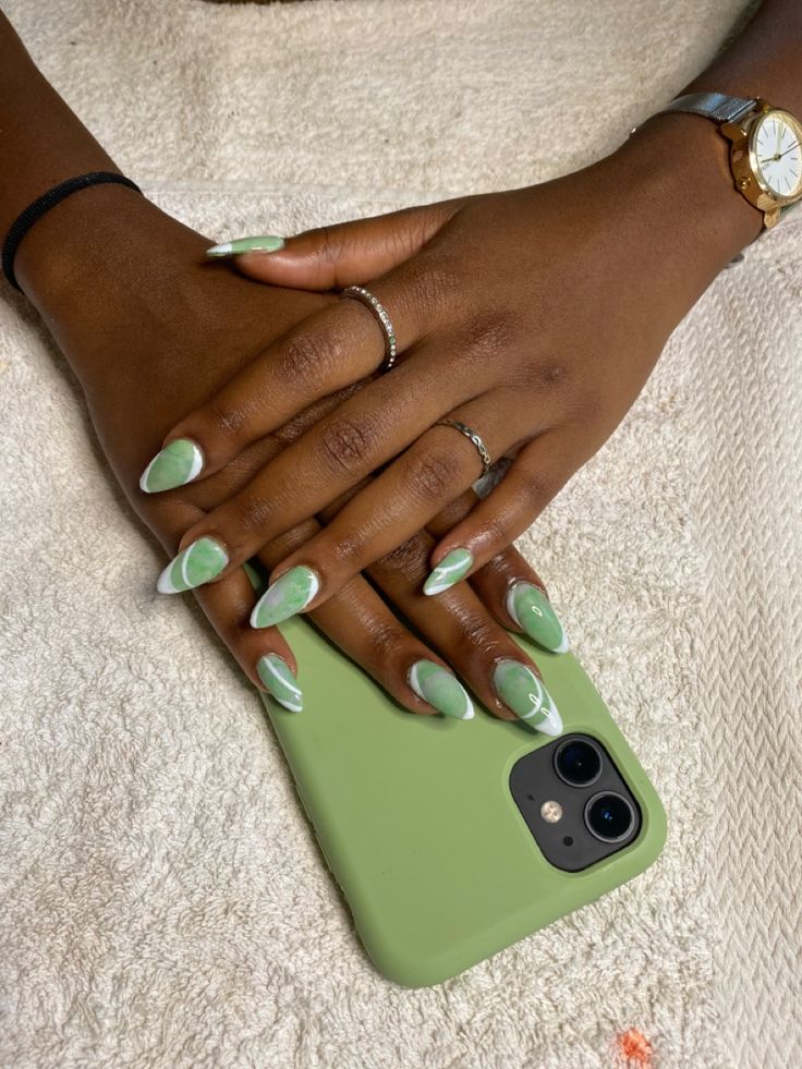 Chic Almond-Shaped Green Nails with White Tips and Marble Effect, Enhanced by Silver Rings.