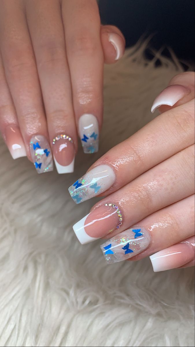 Charming Elegant Nail Design with French Tips, Blue Stars, Glitter, and Glamorous Gem Accents.