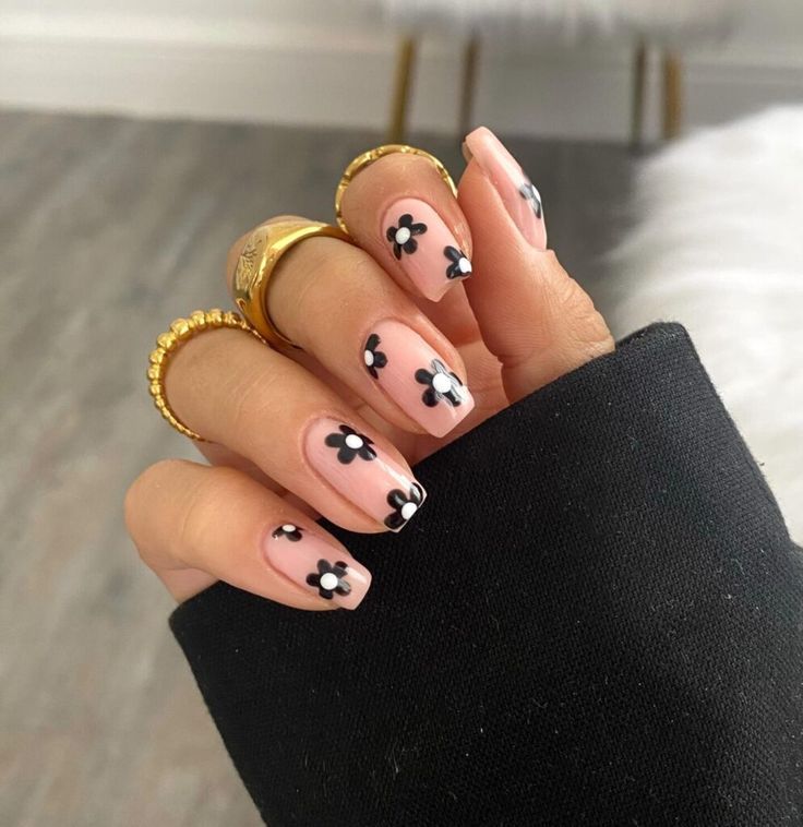 Elegant Floral Nail Design: Soft Nude Base with Chic Black Accents and Gold Rings.