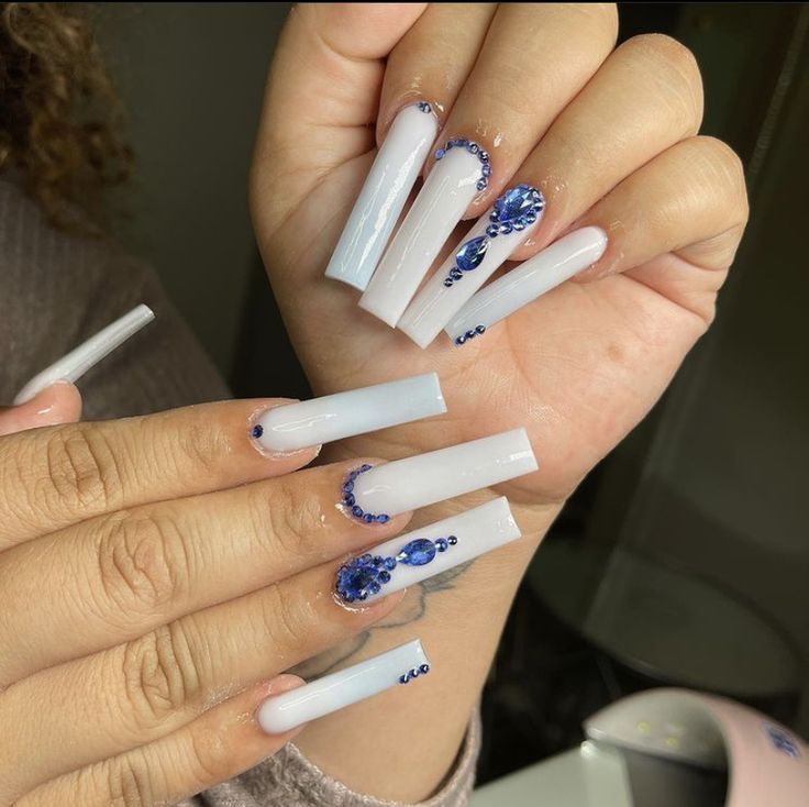 Sophisticated Long Acrylic Nails with Pristine White Base and Intricate Blue Gemstone Accents.