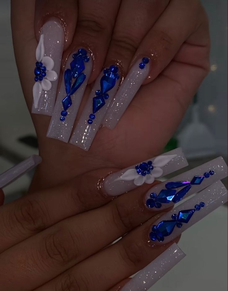 Elegant Blue Gemstone Nail Art with Floral Accents and Shimmering Glitter.