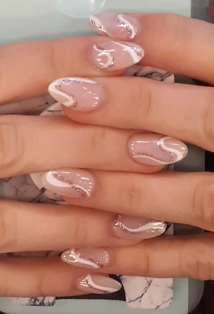 Chic Nude and Glossy White Nail Design with Elegant Swirls and Silver Glitter Accents.