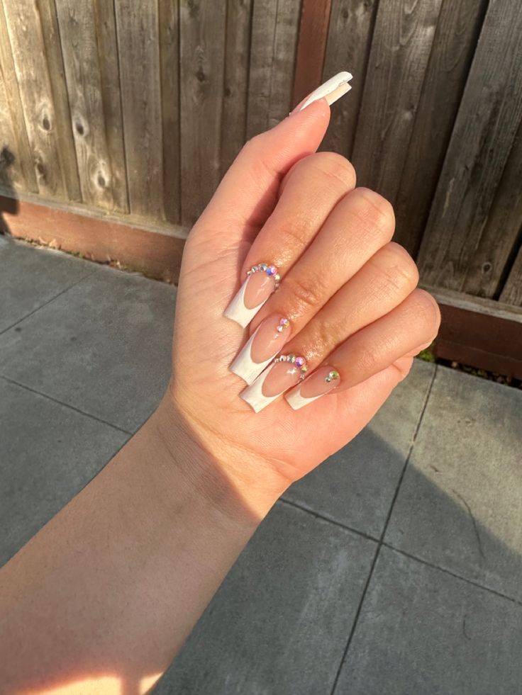 Chic Nude and White Tipped Long Nails Adorned with Sparkling Rhinestones and Colorful Gems.