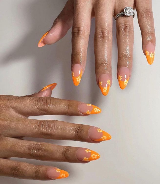 Playful Orange-Tipped Nail Design with Floral Accents for a Trendy Summer Aesthetic.