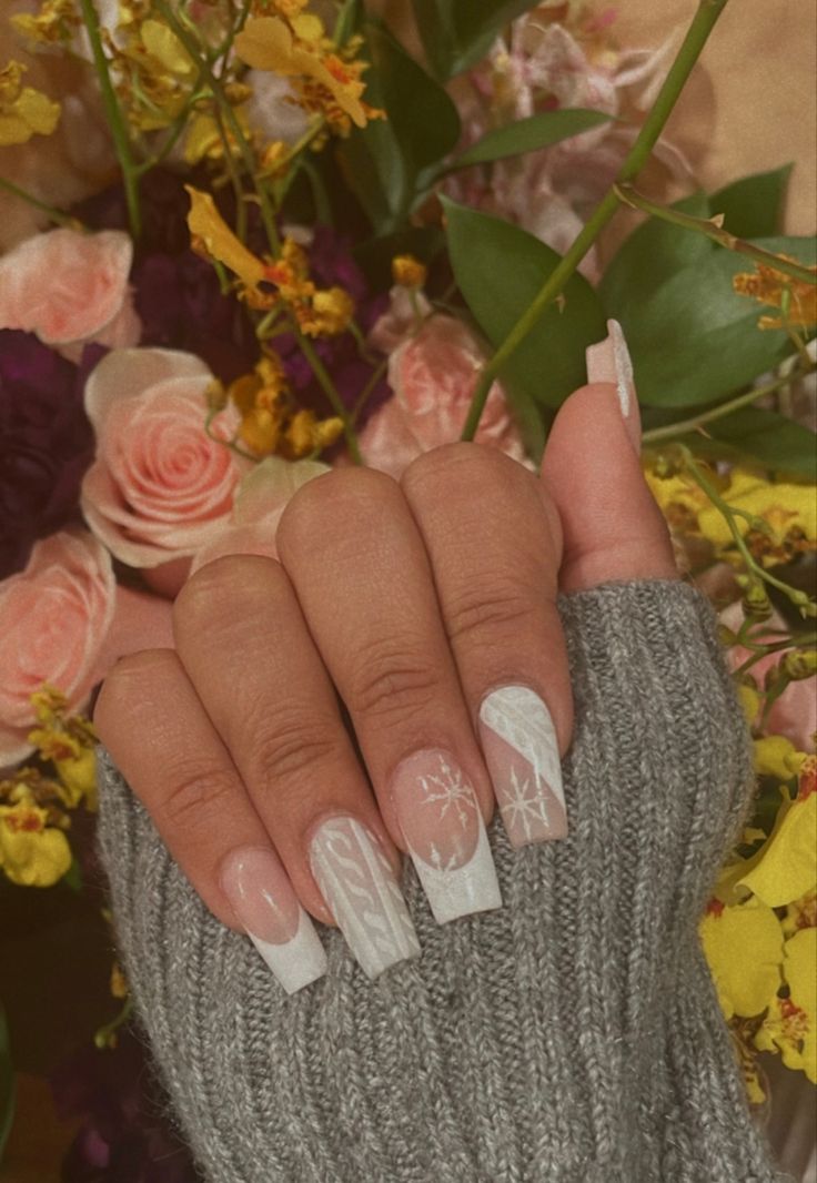 Elegant Nude and White Gradient Nail Design with Hand-Painted Floral and Snowflake Accents, Perfectly Complemented by a Cozy Gray Sweater and Vibrant