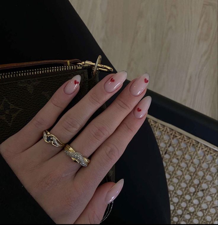 Chic Nude Nail Design with Delicate Red Heart Tips and Gold Ring Accents.