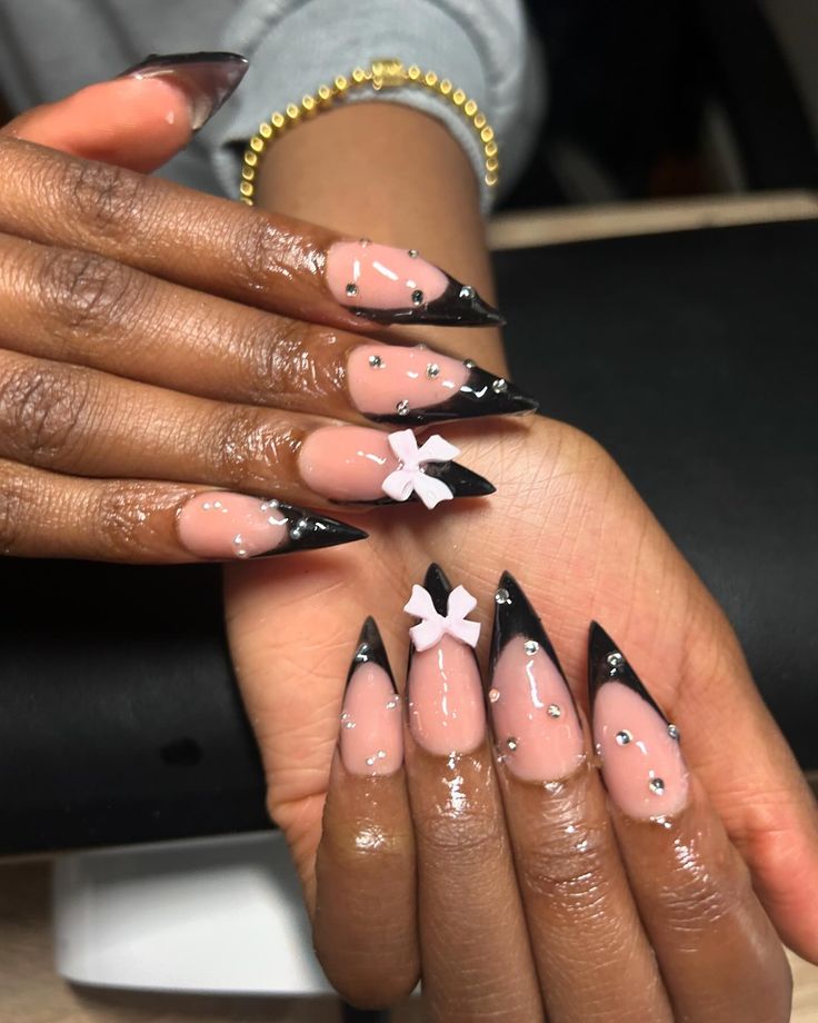 Chic Stiletto Nails: Bold Black Tips with Nude Base, Adorned by Silver Studs and White Bows.