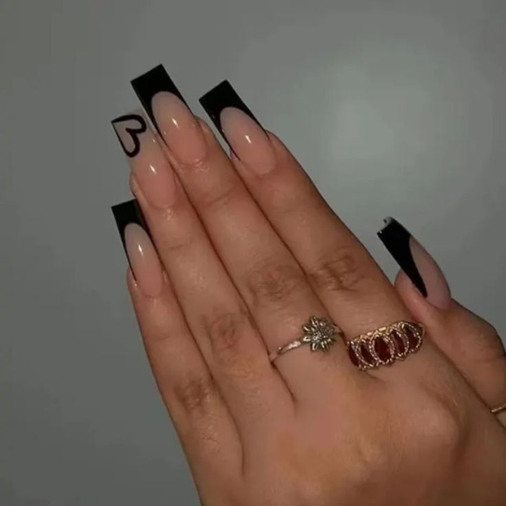 Chic Black and Nude Long Nail Art with Heart Accent and Delicate Rings.