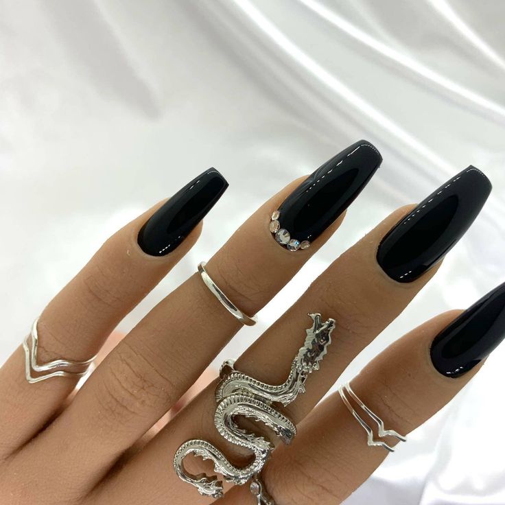 Sleek Black Nail Design with Sparkling Accents and Edgy Silver Rings