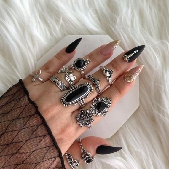 Sophisticated Long Pointed Nail Design in Matte Black with Glittering Gold Accents and Silver Rings.