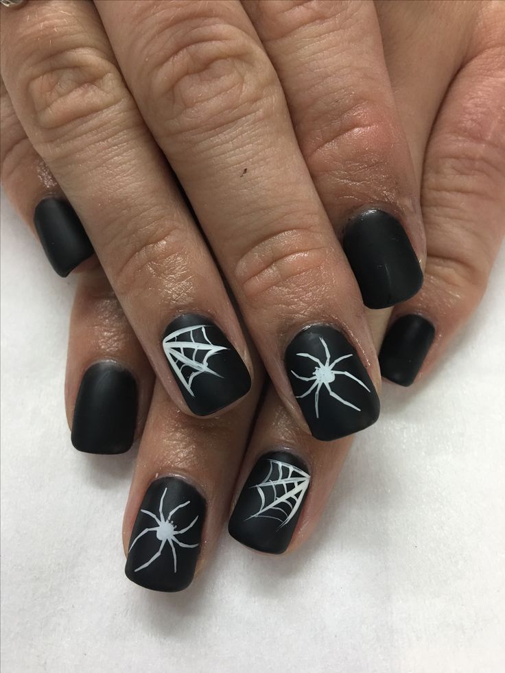 Haunting Glossy Black Nail Art with White Spider and Web Designs for Halloween.