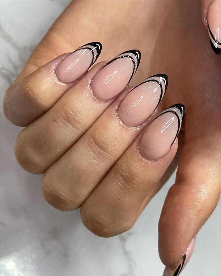 Chic Almond-Shaped Nude Nails with Artistic Black Tips for a Modern French Manicure.