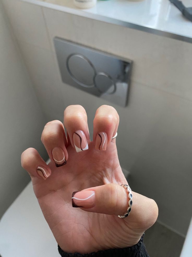 Chic Nude and White Nail Design with Wavy Patterns and French Tips, Accented by a Silver Ring.