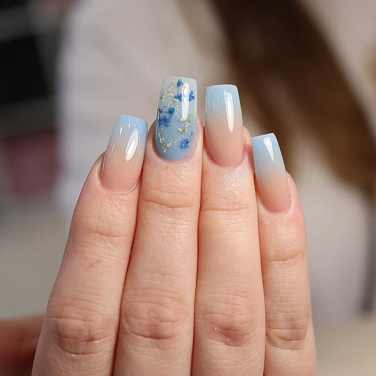 Trendy Ombre Nail Design with Soft Blue Hues and Floral Accents for a Serene Elegance.