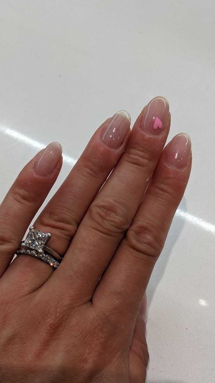 Chic Nude Nail Design with Minimalist French Tips and Playful Pink Heart Accent.