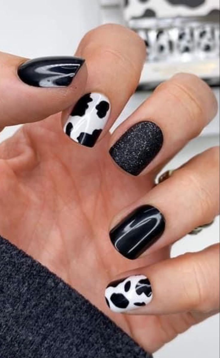 Chic Black and White Nail Design with Playful Cow Print and Glittery Accent.