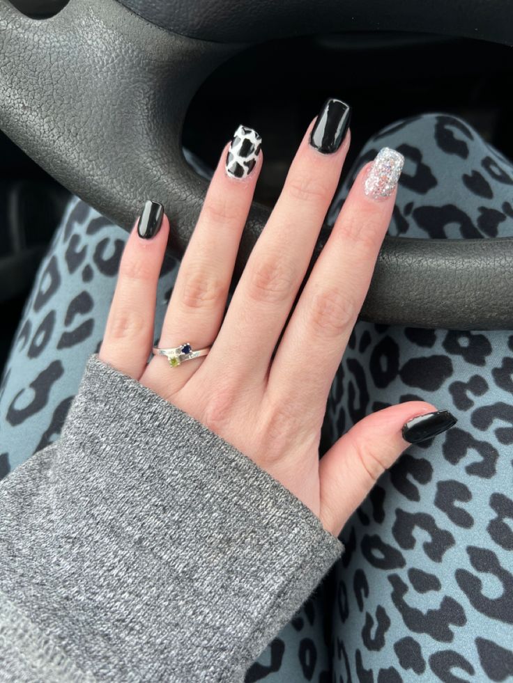 Bold and Trendy Nail Design Featuring Glossy Black, Sparkling Silver, and Playful Cow Print.