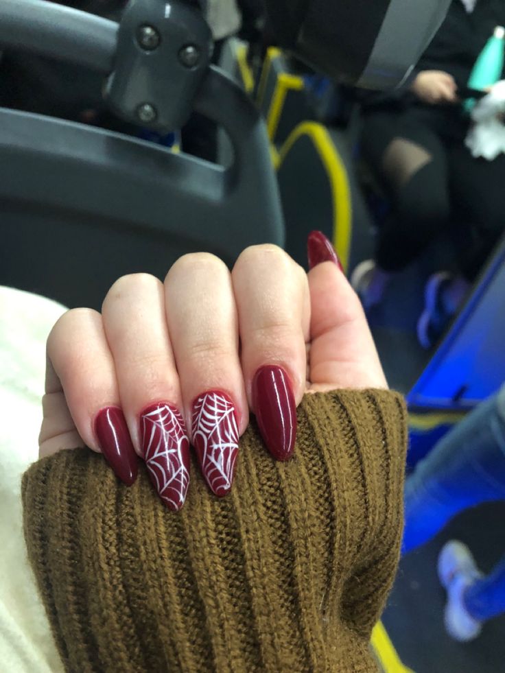 Striking Burgundy Nails with Intricate White Spiderwebs Perfectly Complement Cozy Sweater Styles.