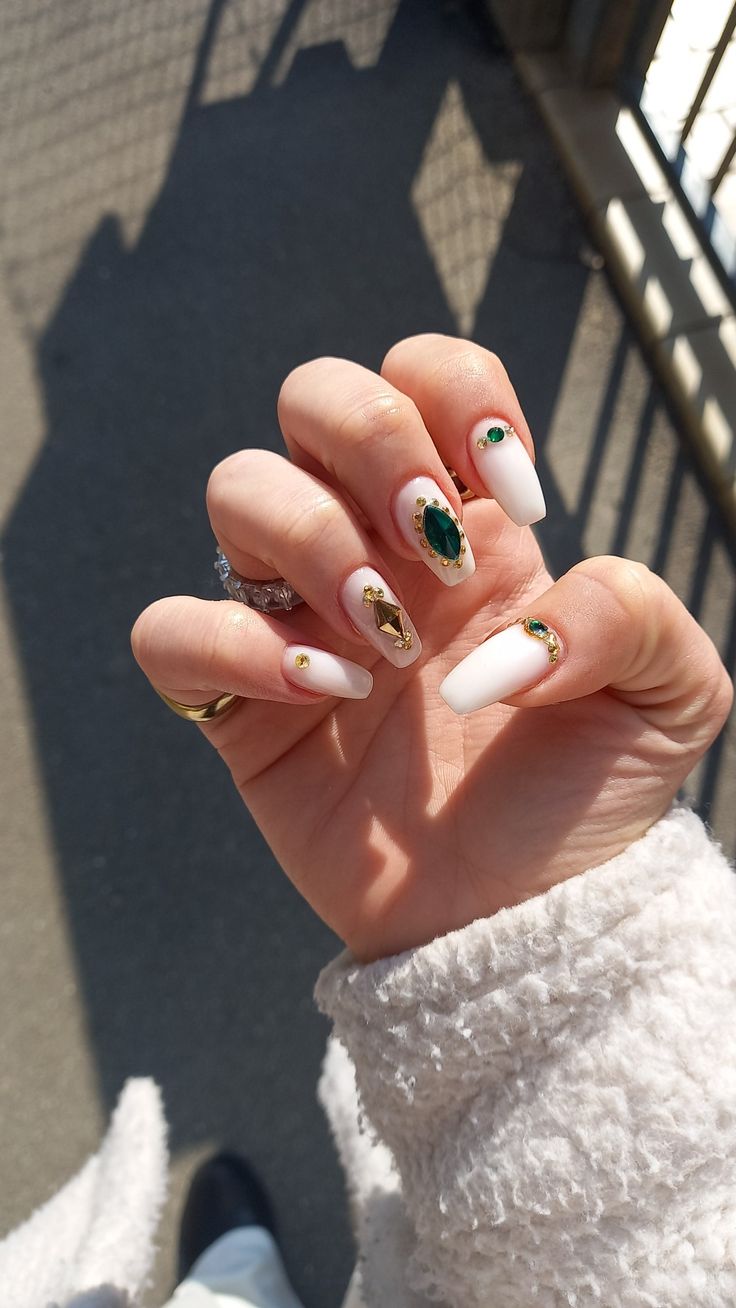 Sophisticated Nail Design: Glossy White Base with Gold Accents and Green Gemstones.