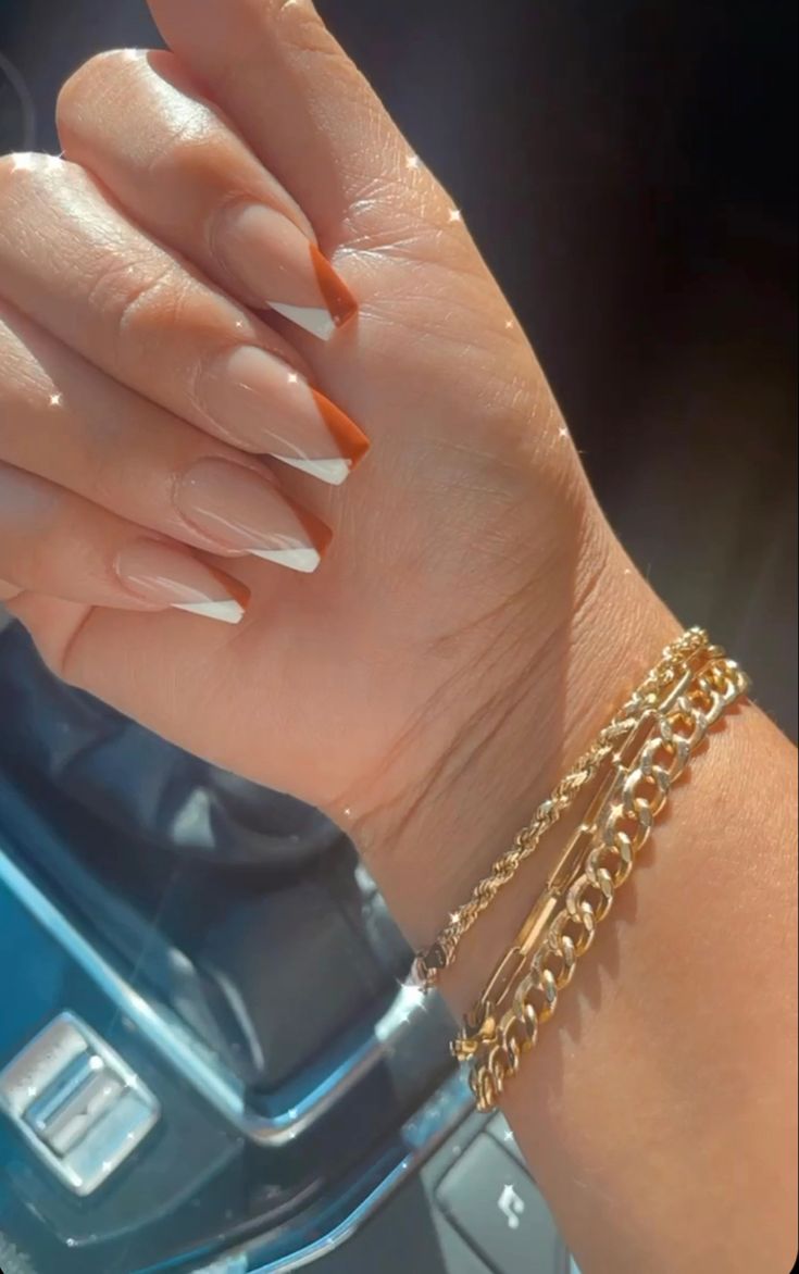 Elegant French Tip Nail Design with Orange Accent and Gold Bracelet Styling.