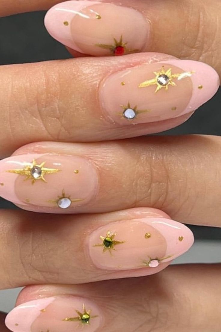 Glamorous Nail Design: Soft Pink Base with Golden Starbursts and Colorful Gems.