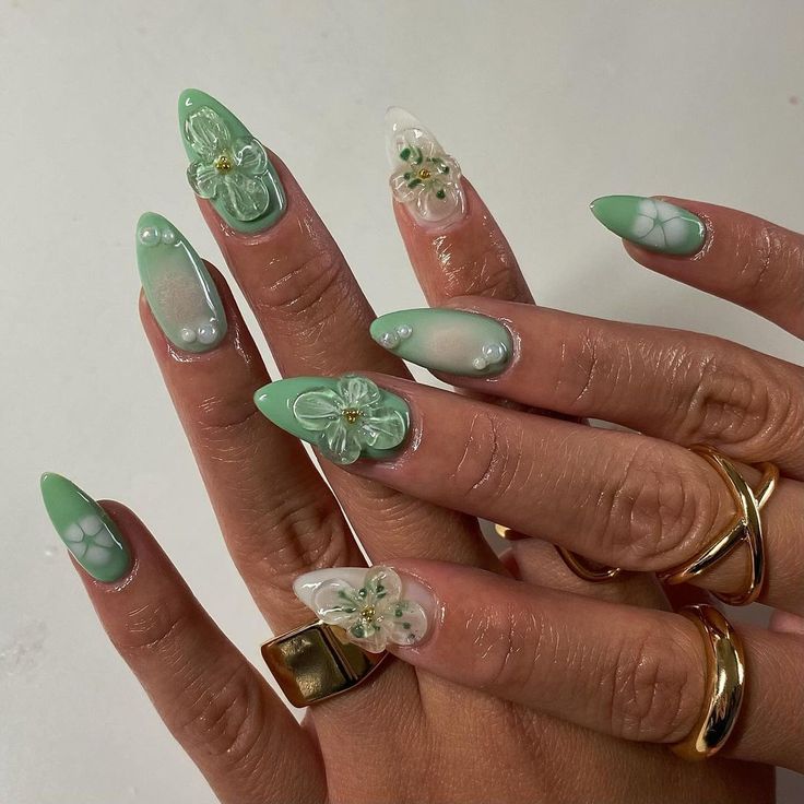 Chic Soft Green Stiletto Nail Design with Floral Motifs and Gemstone Accents.