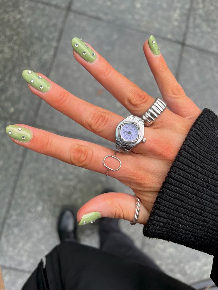 Trendy Green Nail Design with Subtle Rhinestones and Elegant Rings for a Chic Look.