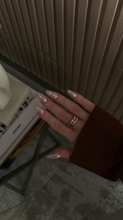 Chic Almond-Shaped Nails with Nude Polish and Golden Rings Create Understated Glamour on a Sleek Glass Table.