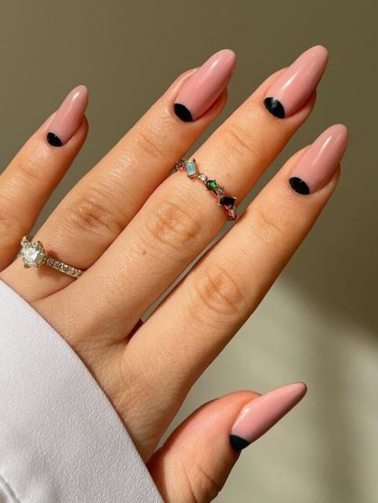 Elegant Soft Pink Nail Design with Black Half-Moon Accents and Delicate Rings.