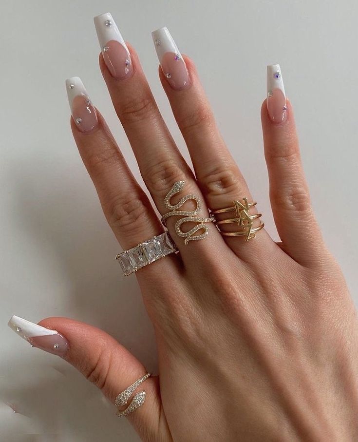 Elegant French Tip Nails with Gemstone Accents and Chic Statement Rings.