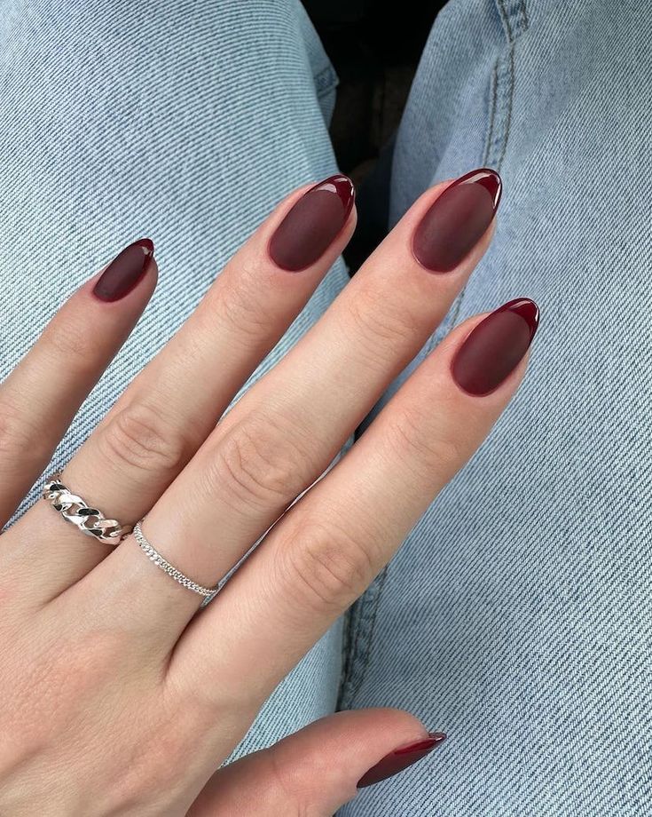 Sophisticated Burgundy Almond Nails with Glossy Tips and Matte Finish, Accentuated by Silver Rings.