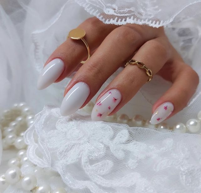 Chic Almond-Shaped Nails with Glossy White Polish and Pink Floral Accents, Enhanced by Gold Rings.