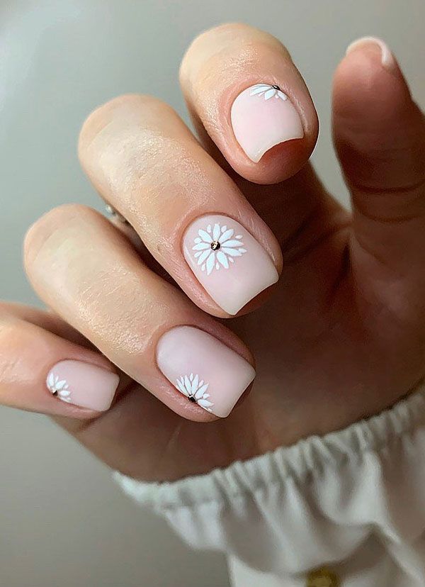 Chic Soft Pink Nail Art with Delicate White Daisy Patterns and Subtle Embellishments.