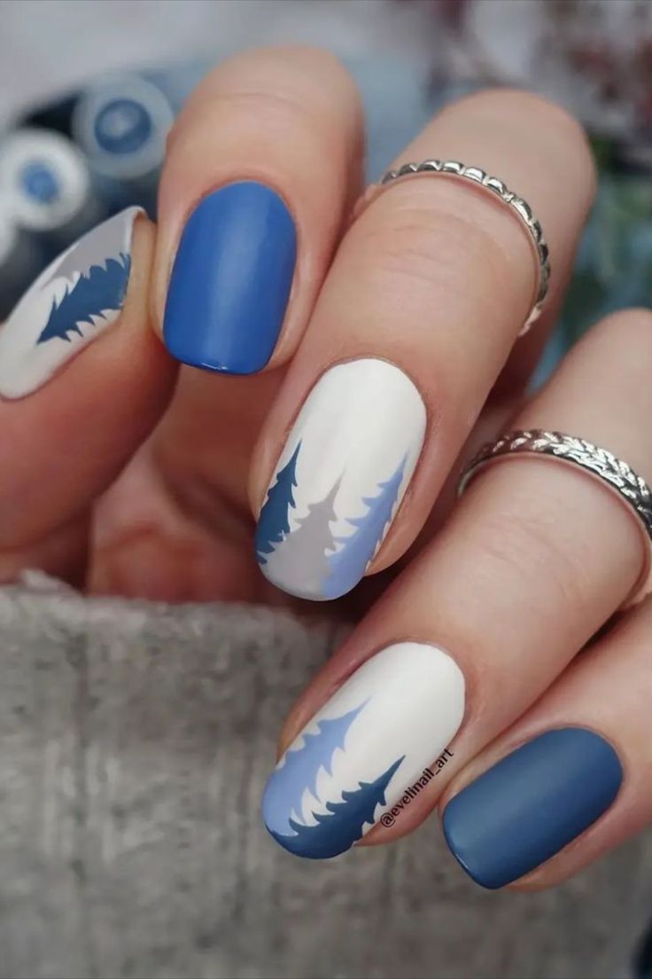 Elegant Blue and White Matte Nail Design with Whimsical Tree Silhouettes on a Neutral Background.